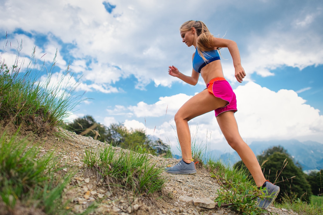 Young Blonde Girl Athlete Running In The Mountains Uphill On Tra